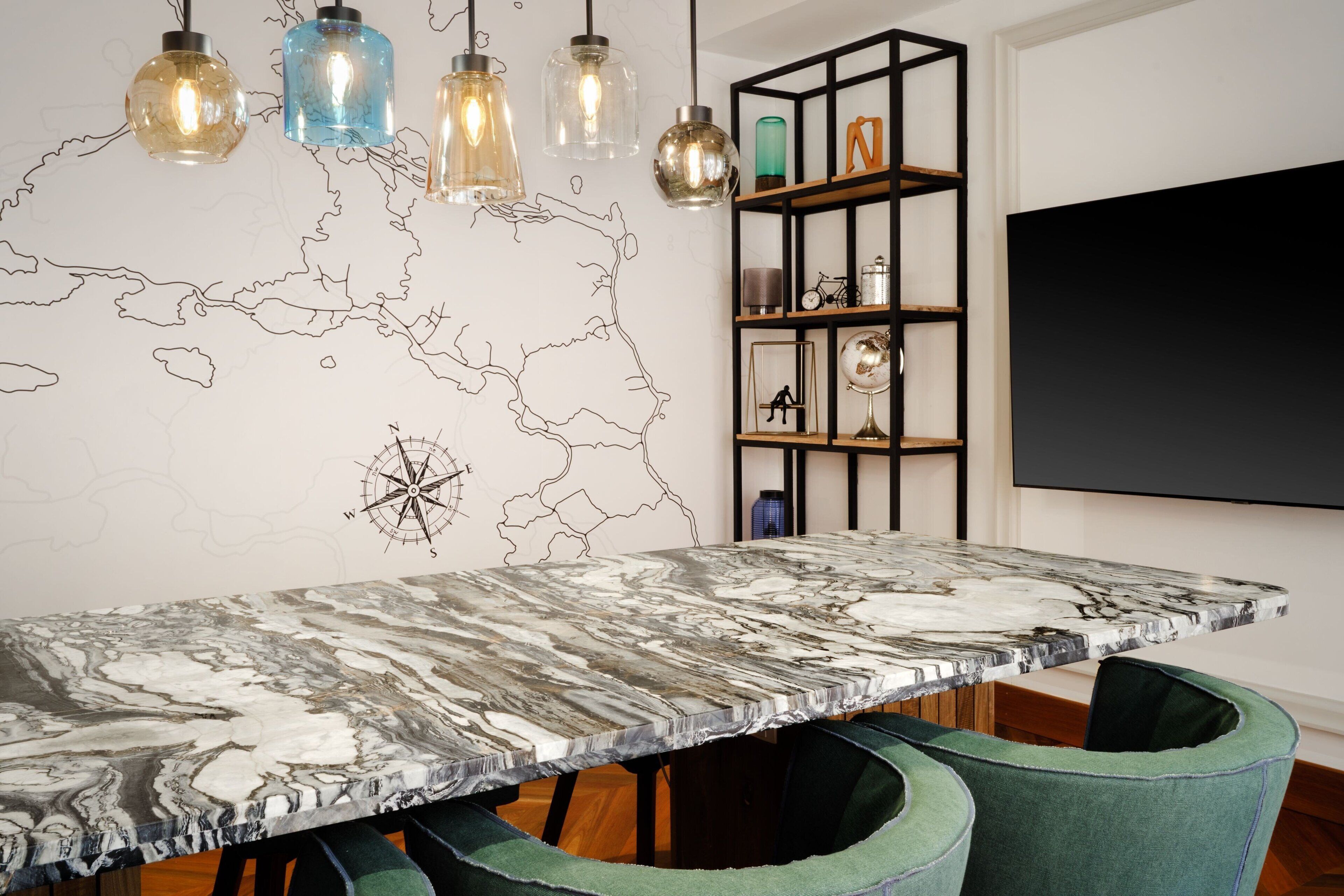 Un comedor con una mesa de mármol, sillas tapizadas en verde, lámparas colgantes, una pizarra y un mapa del mundo en la pared.