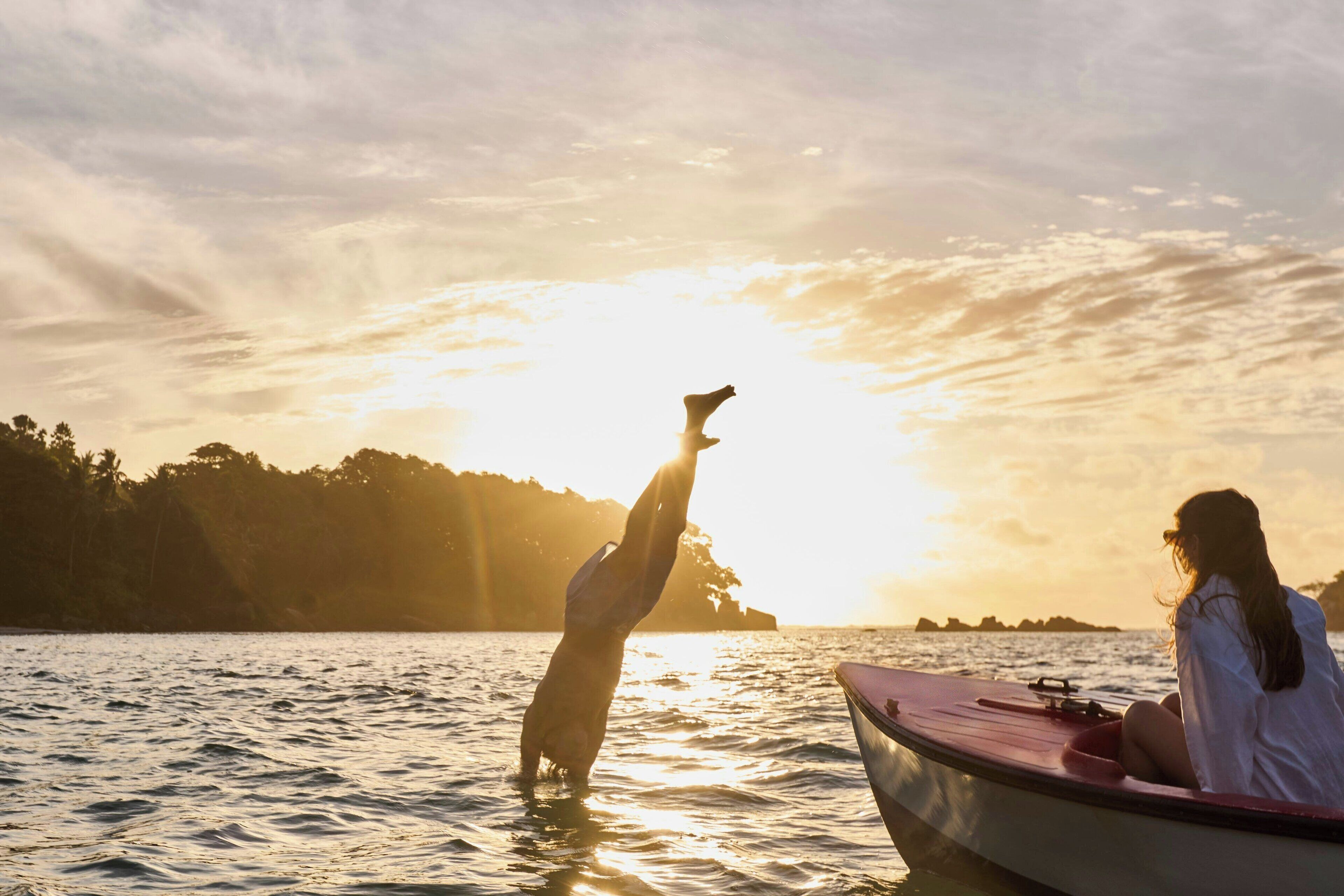 A sunset over a body of water with a person standing in the water and another person in a boat.