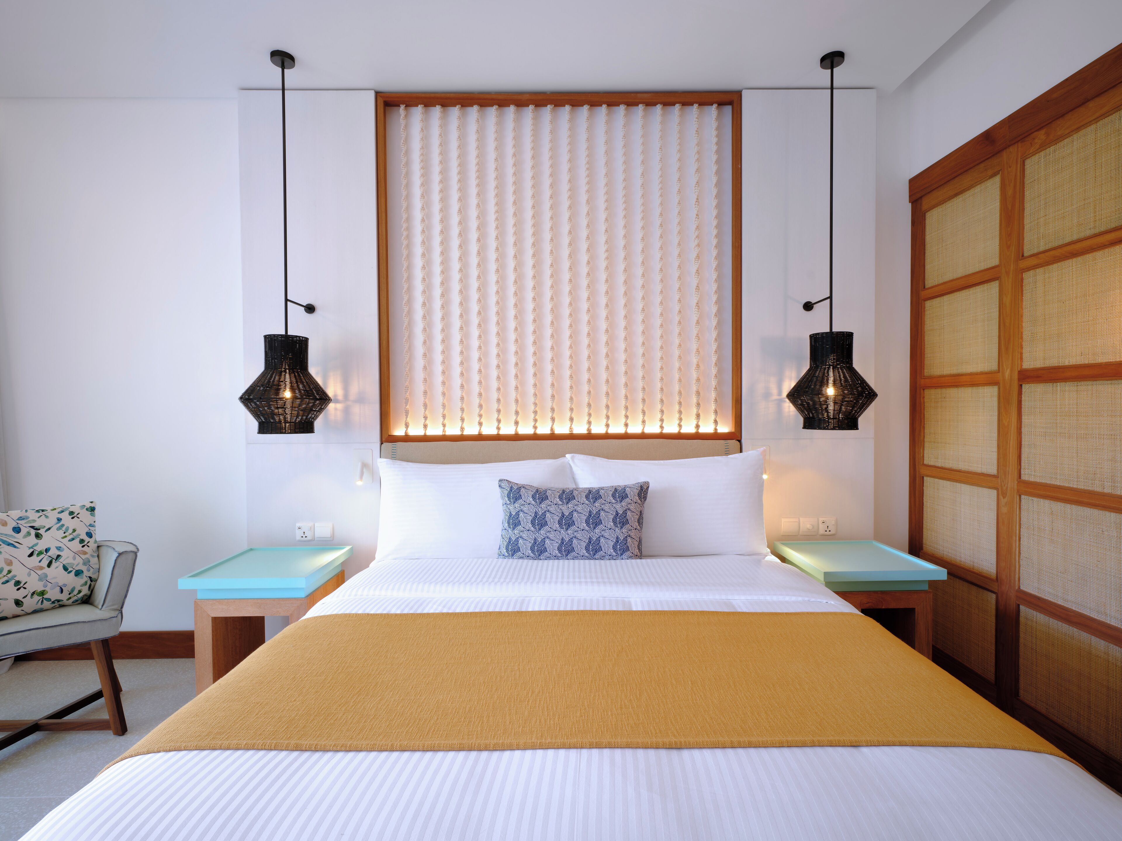 A neatly arranged hotel room with a large bed, two bedside tables, a chair, and a traditional-style partition.
