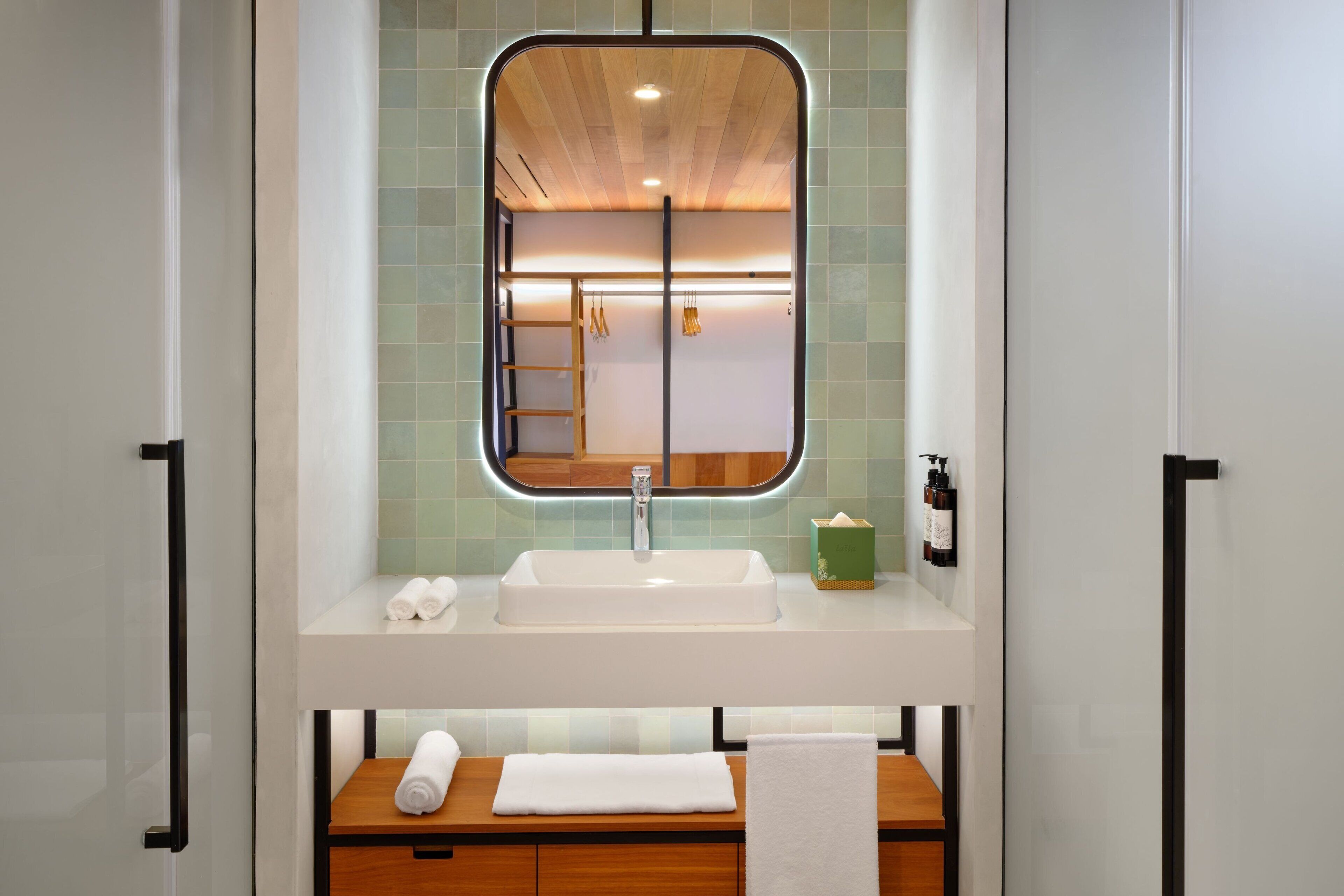 Une salle de bain avec un lavabo blanc, un miroir et un meuble-lavabo en bois.