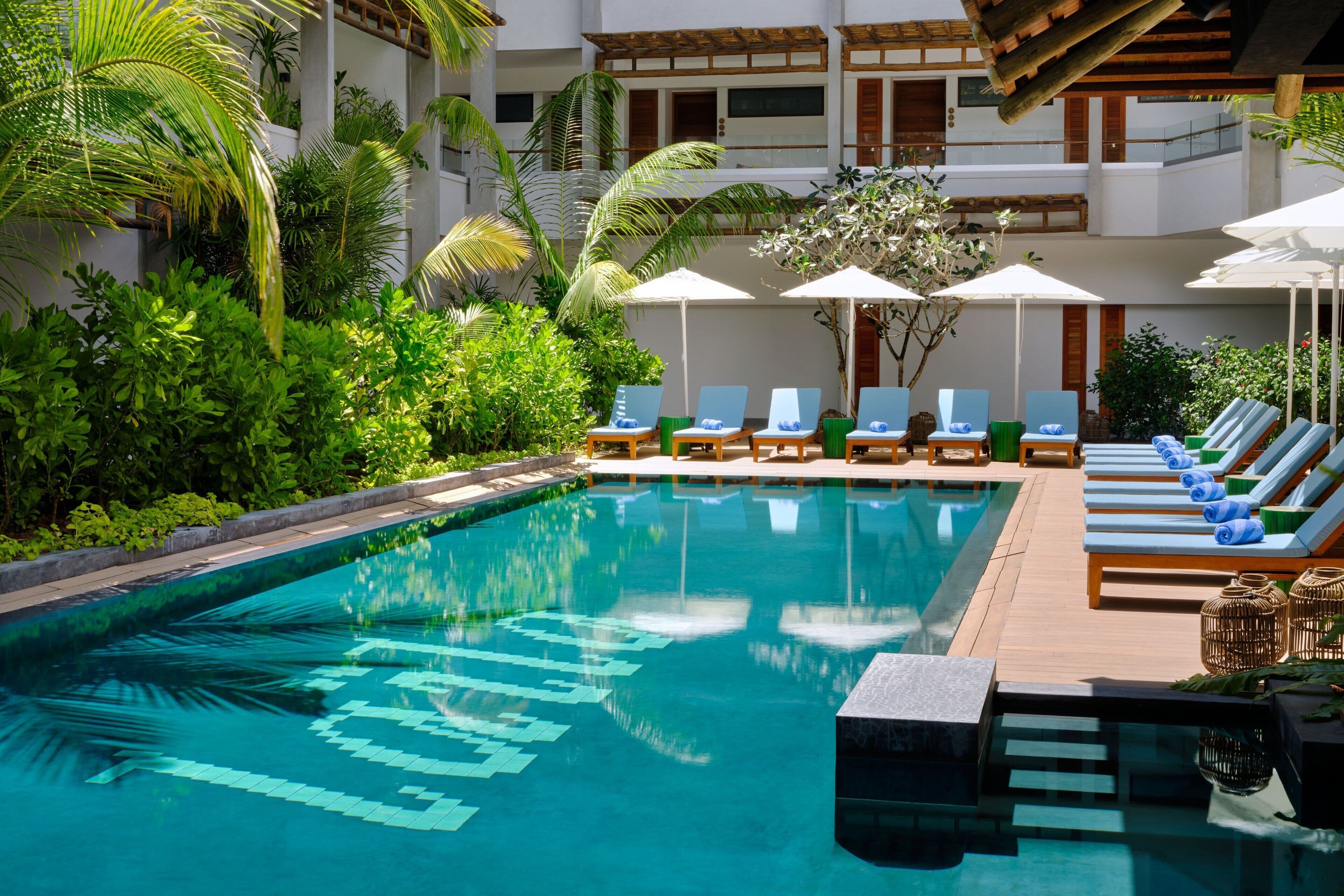 Zona de piscina con sillas de descanso y sombrillas, rodeada de exuberante vegetación.