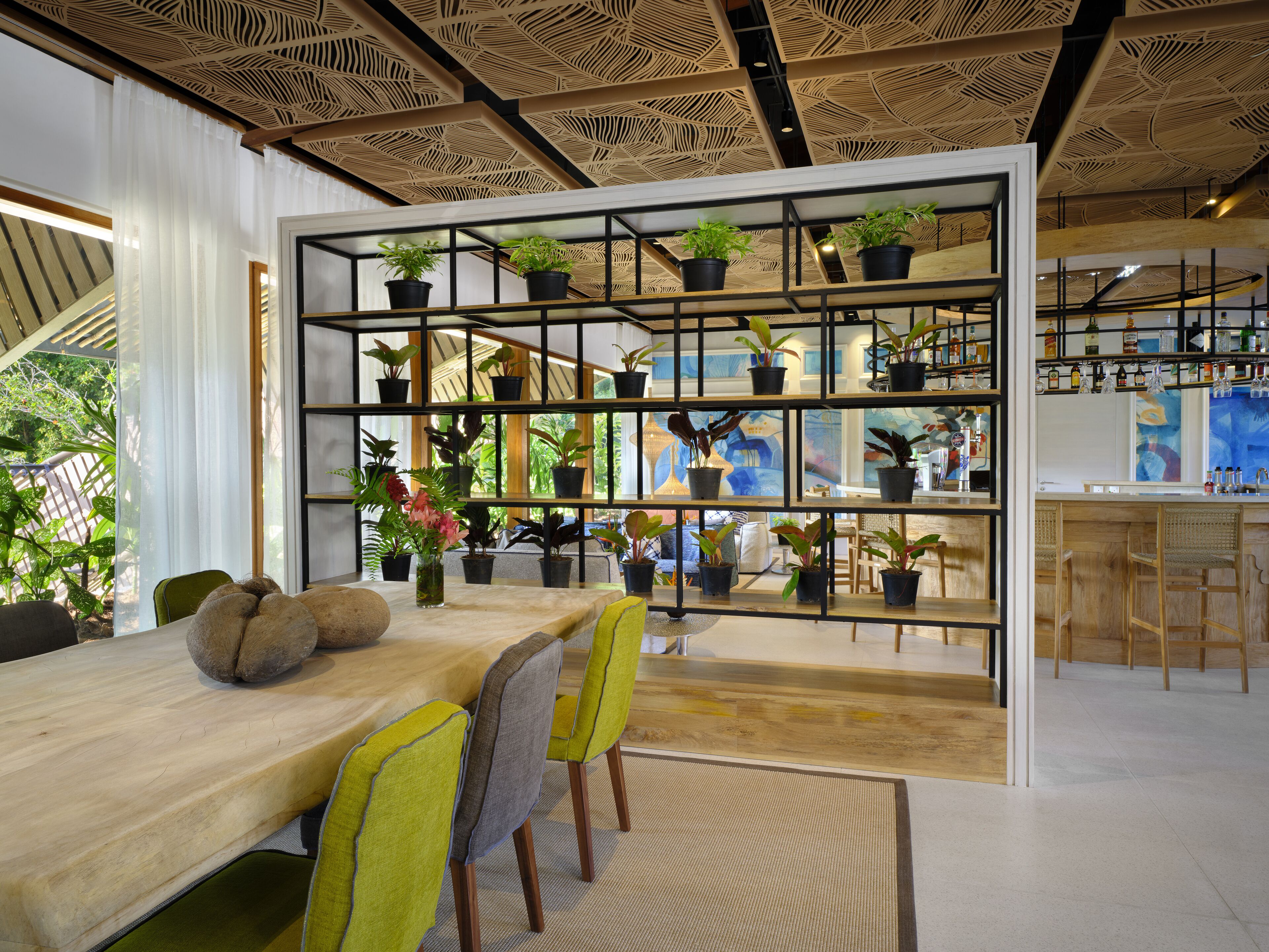 A modern dining area with a wooden table, yellow chairs, and a plant-filled shelving unit.