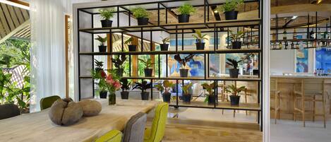 Uma sala de jantar moderna com uma mesa de madeira, cadeiras amarelas e uma estante cheia de plantas.