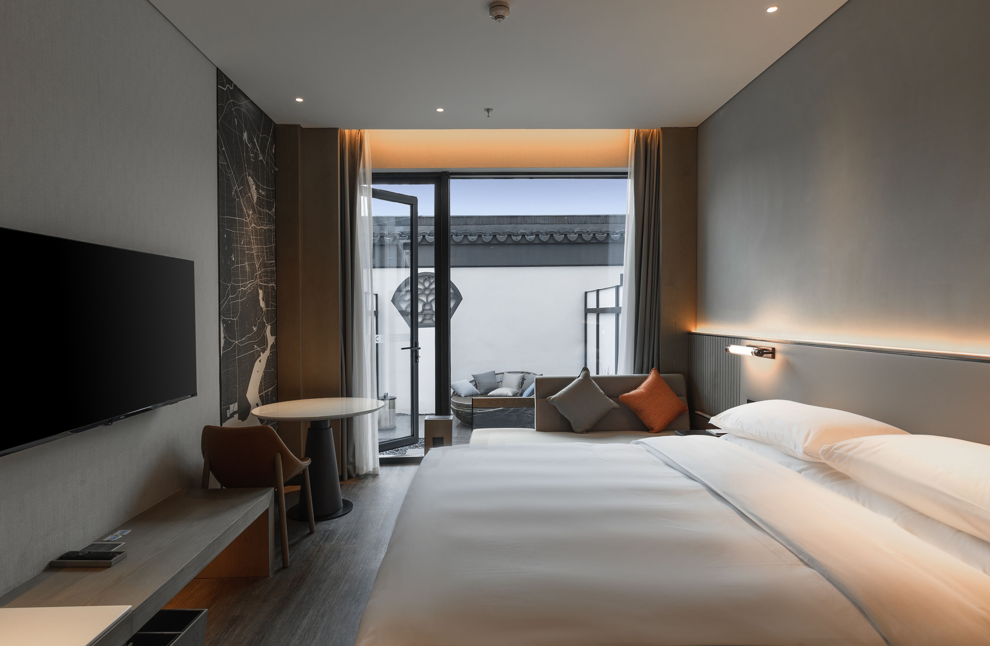 A modern hotel room with a large bed, a desk, a flat-screen TV, and a balcony with a view of the city.