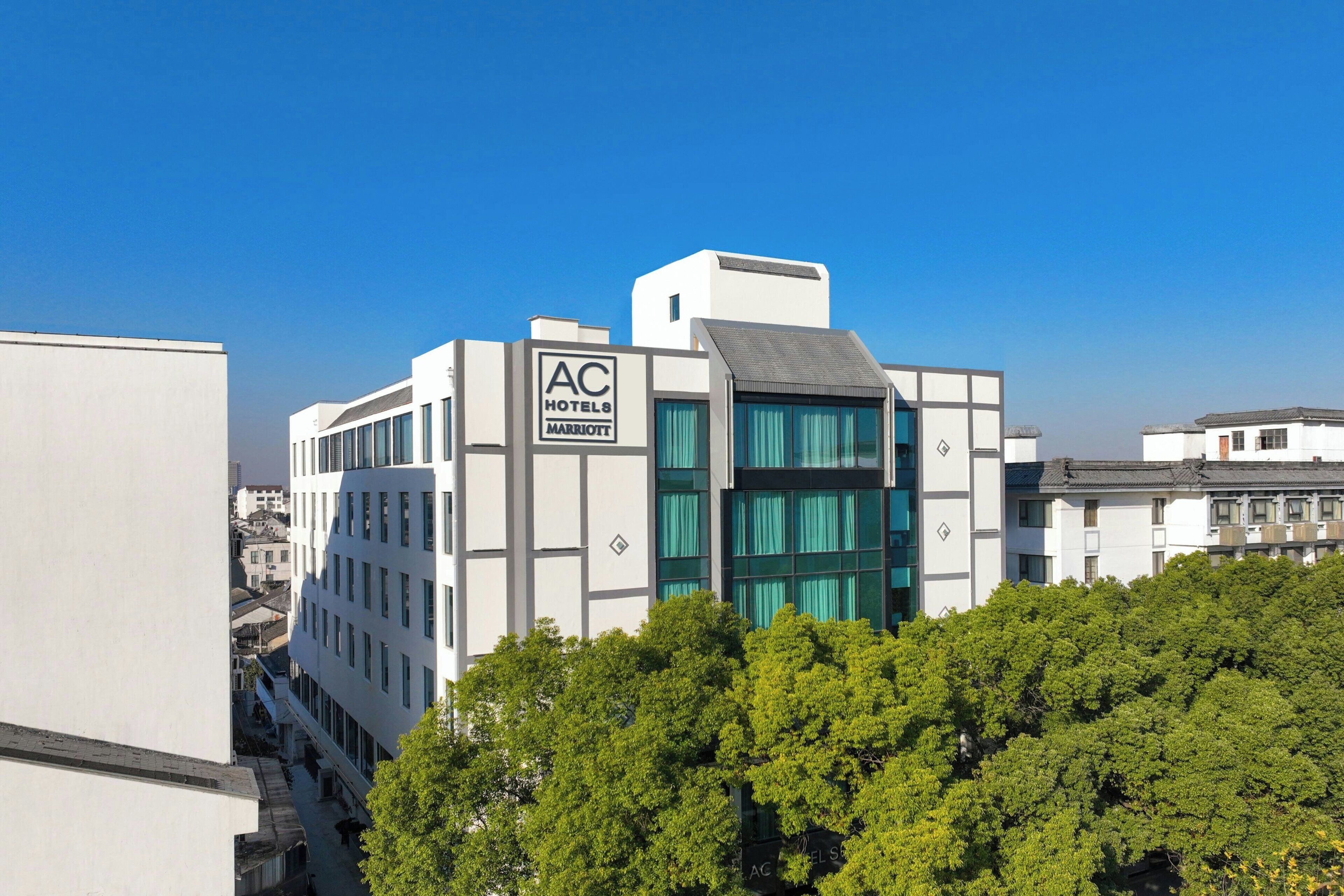 A modern hotel building with a sign for AC Hotels Marriott, featuring a prominent glass facade and a flat roof.