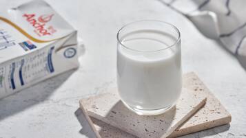 Ein Glas Milch auf einem Untersetzer, im Hintergrund eine Milchpackung.