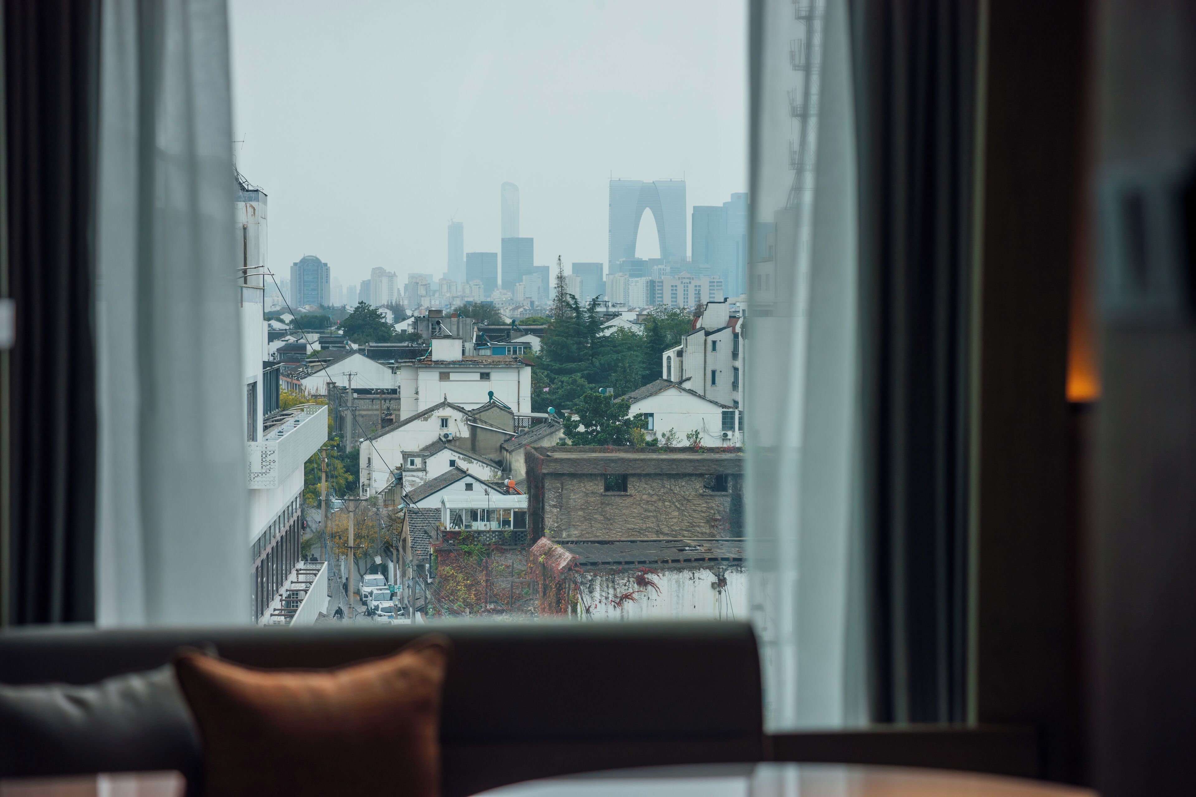 A view from a window of a cityscape with buildings and a prominent arch structure in the distance.