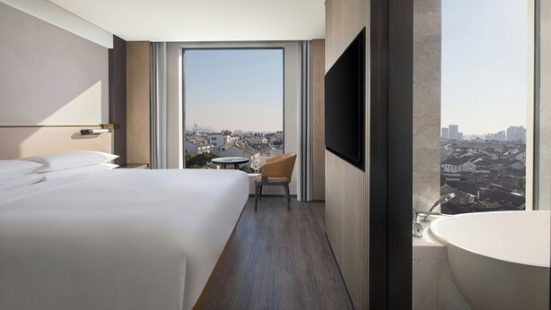 Una habitación de hotel moderna con una cama grande, televisión, baño con bañera y vistas a la ciudad.