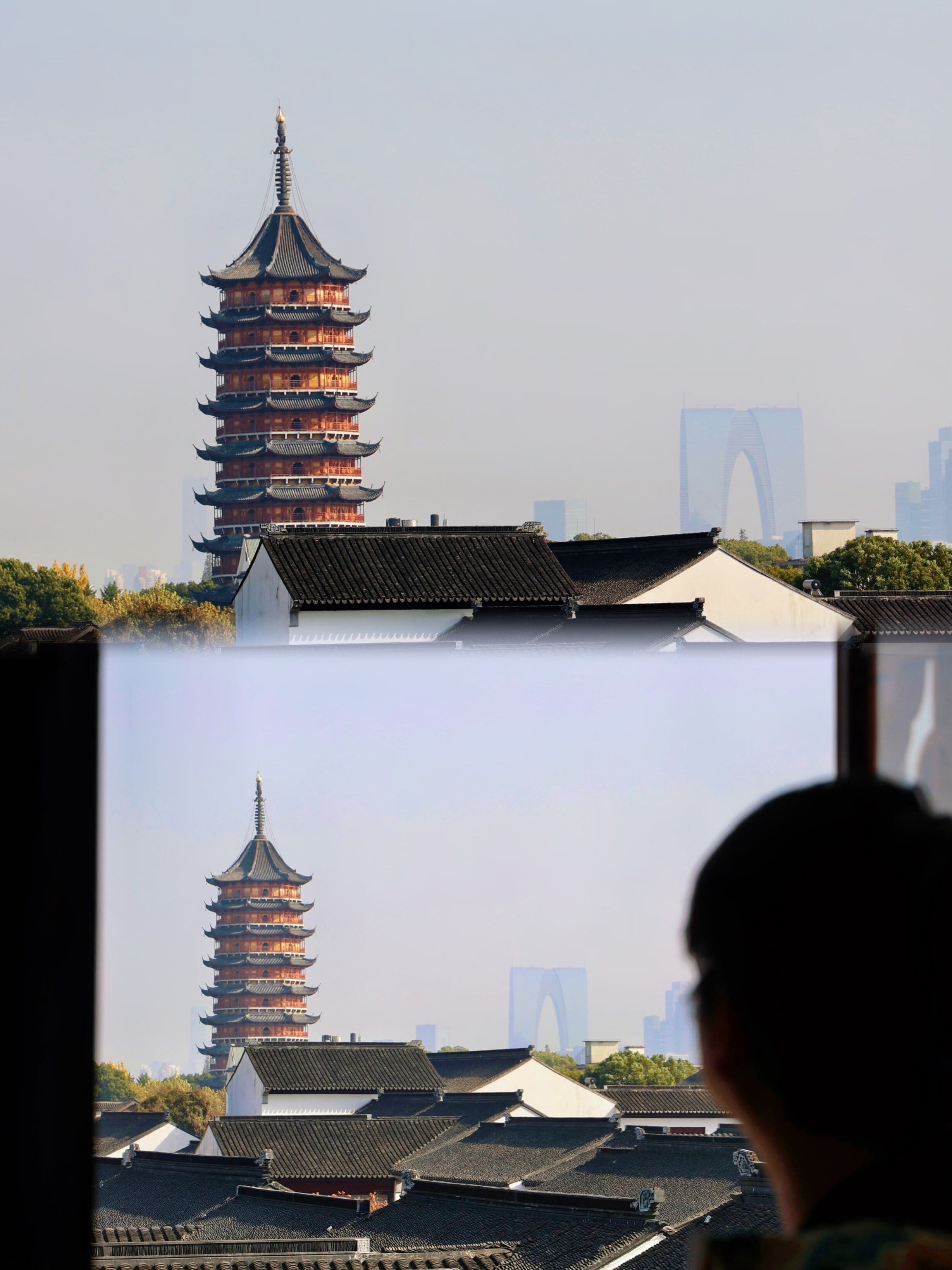 A traditional pagoda-style building with multiple tiers, surrounded by other traditional architecture and modern buildings in the background.