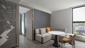 Een moderne woonkamer met een hoekbank, een ronde tafel en uitzicht op de stad door grote ramen.