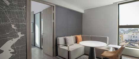 Una sala de estar moderna con un sofá seccional, una mesa redonda y vistas de la ciudad a través de grandes ventanales.
