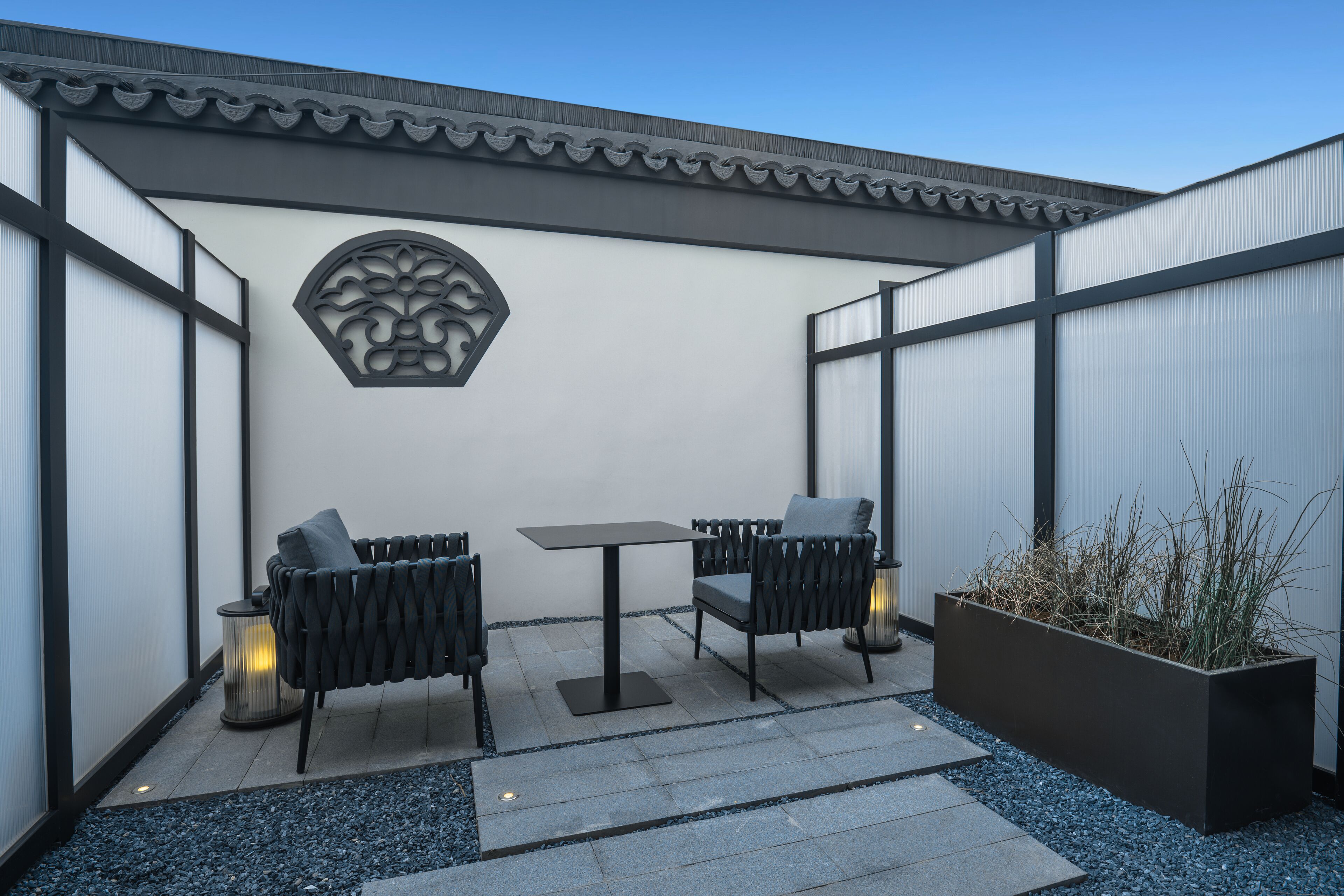 Een terras buiten met twee zwarte stoelen, een tafel en een decoratief wandobject.