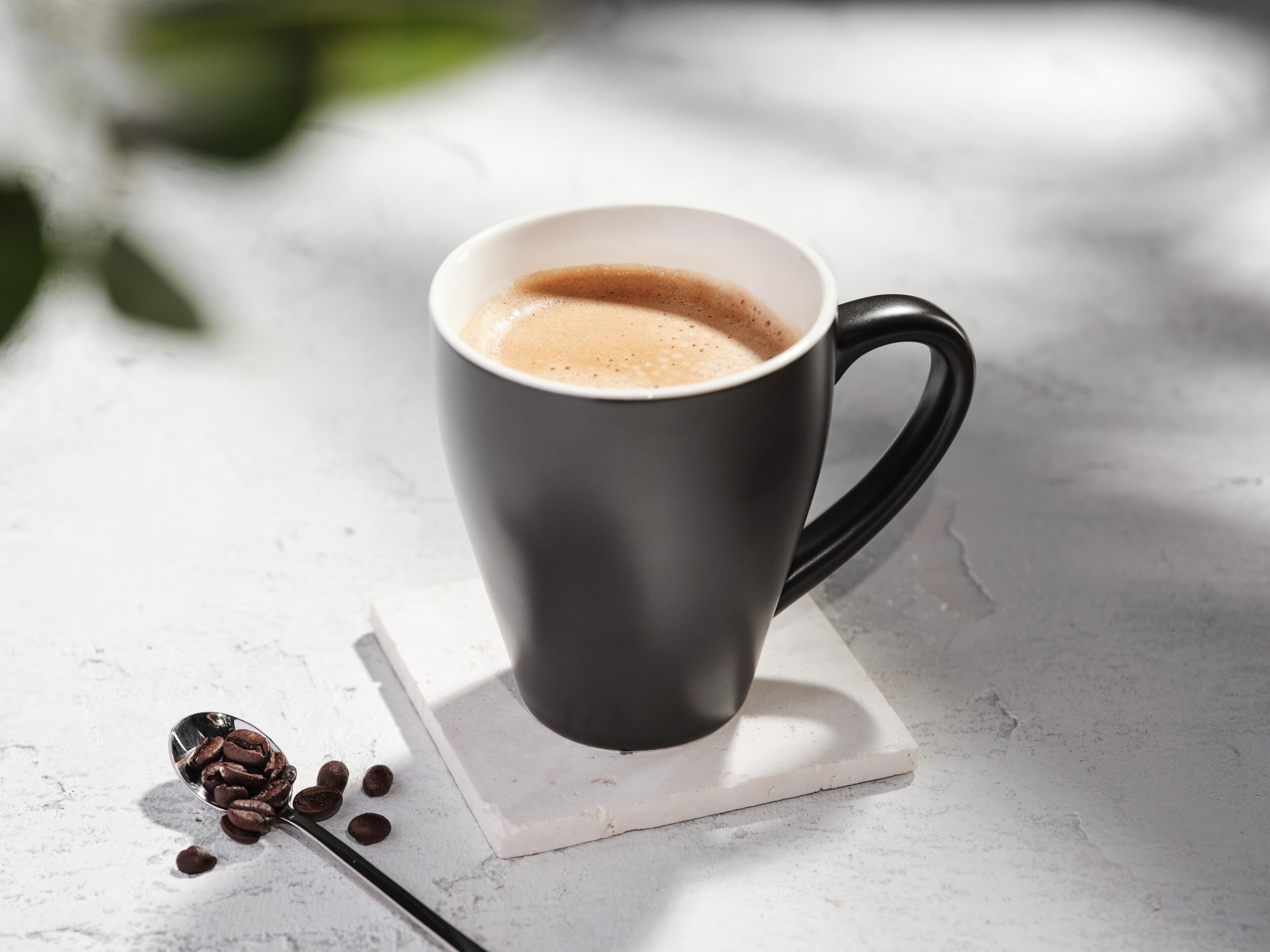 Une tasse de café noir posée sur un sous-verre blanc, avec des grains de café à côté.