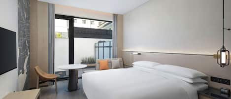 A modern hotel room with a large bed, a desk, a chair, and a small table.