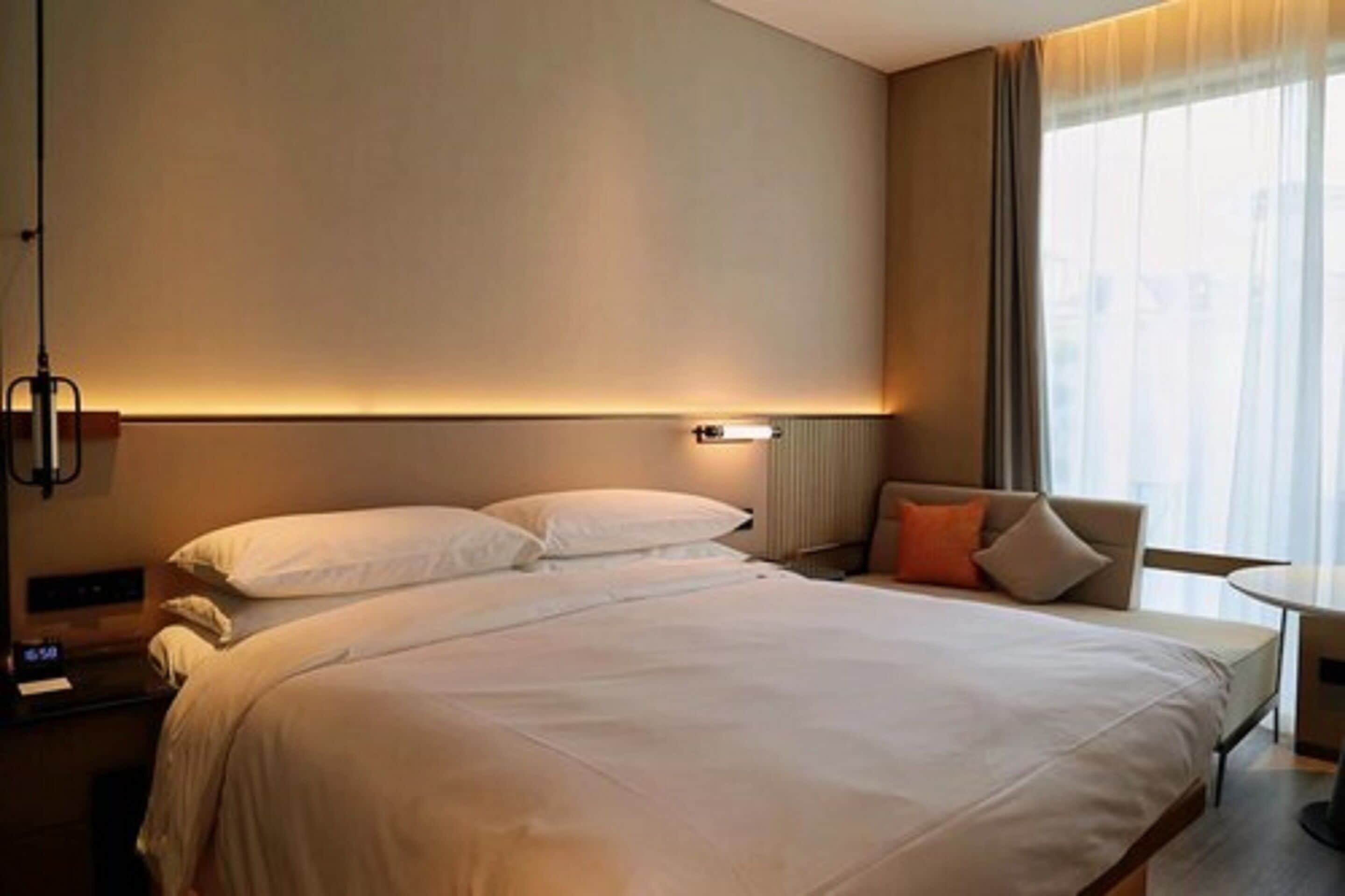 Une chambre d’hôtel avec un grand lit, une table de chevet, une chaise et une fenêtre avec des rideaux.