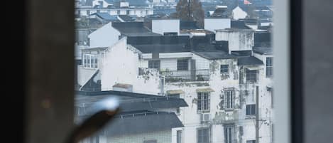 A view from a window overlooking a densely packed urban area with various buildings and a prominent tree.