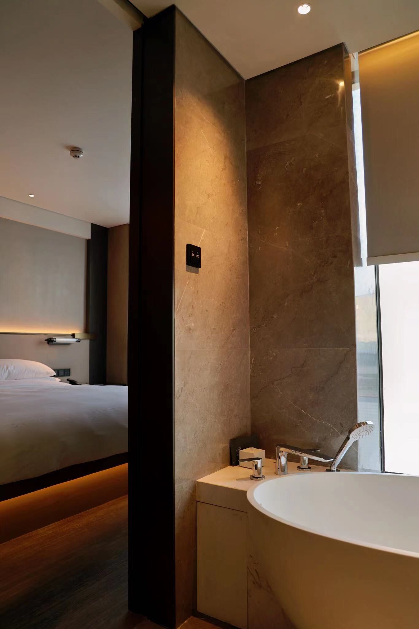 Une salle de bain d’hôtel moderne, dotée d’une grande baignoire, d’un meuble-lavabo avec miroir et d’un lit dans la pièce adjacente.