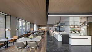 Un restaurante moderno con zona de bar, suelos de madera, ventanas amplias y diversas opciones de asientos.