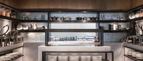 A modern kitchen with marble countertops, stainless steel appliances, and neatly arranged shelves with kitchenware.