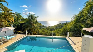 A swimming pool with lounge chairs and umbrellas, surrounded by lush greenery and a view of the ocean. - La Mer Luxury Villa - 3 bdrm with sea view & private pool (Cap Estate)