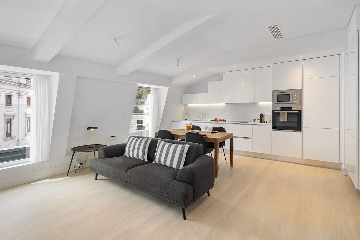 Un appartamento moderno con zona pranzo, cucina e un divano grigio con cuscini a righe.