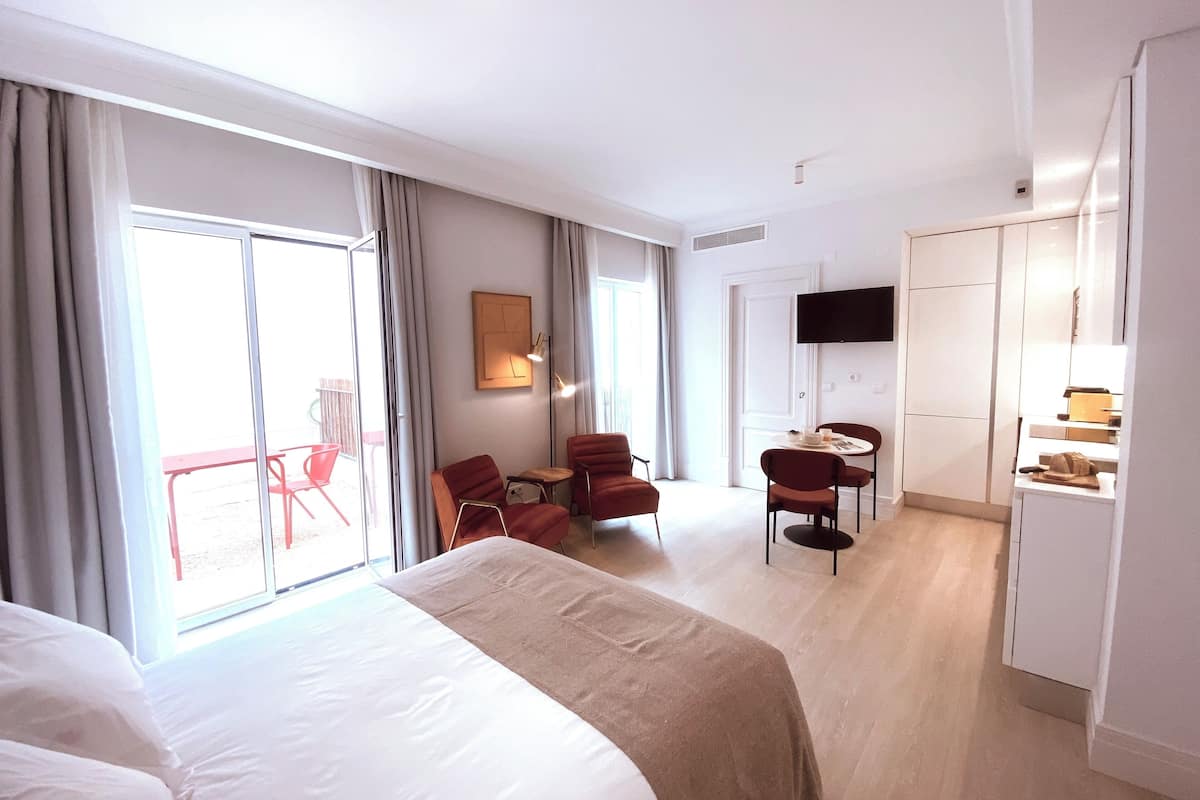 Una camera d'albergo con un letto grande, una scrivania con due sedie, una TV a parete e una porta scorrevole che dà su un balcone.