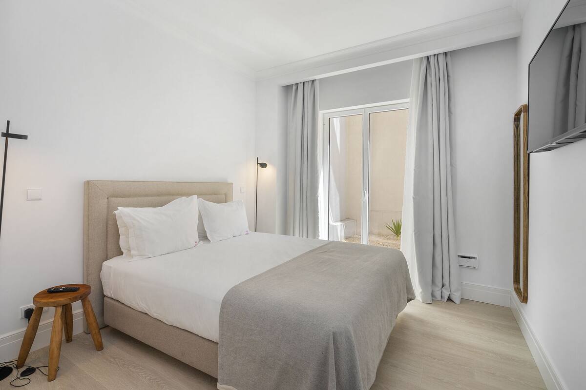 Una camera da letto moderna con un letto, un comodino e un'ampia finestra con tende.