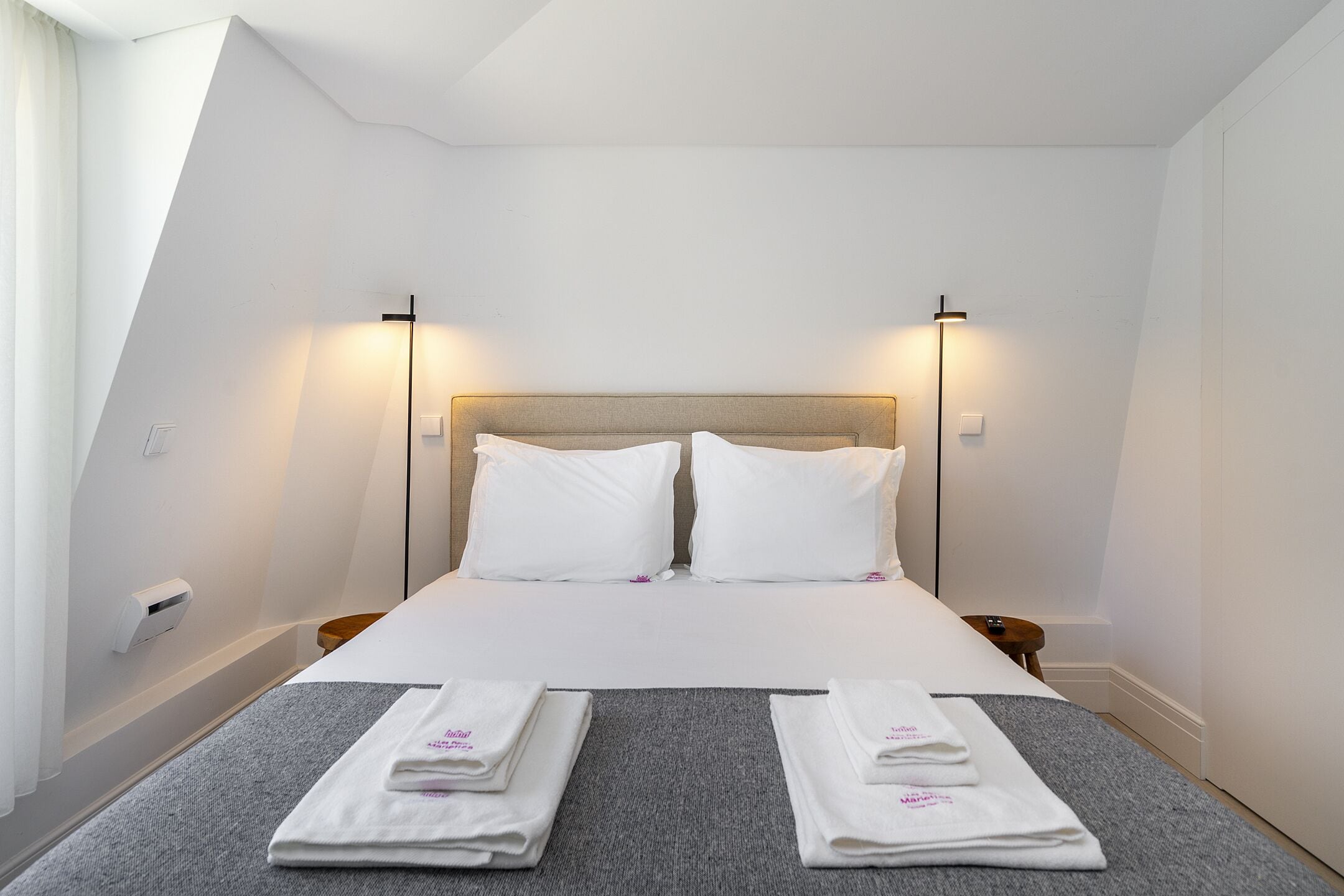 Et hotelværelse med en seng, to sengeborde og lamper samt et foldet håndklæde på sengen.