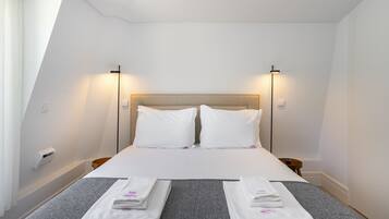 Et hotelværelse med en seng, to sengeborde og lamper samt et foldet håndklæde på sengen.