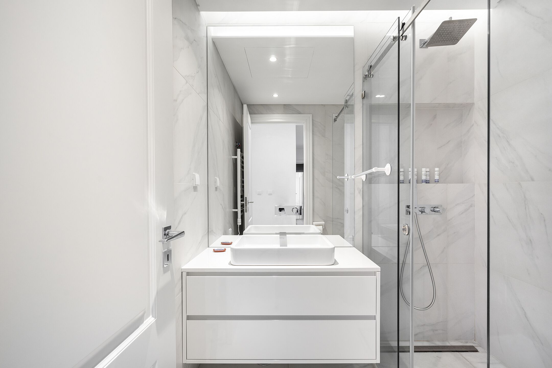 Un baño moderno con ducha de vidrio, tocador blanco con lavamanos grande y espejo sobre el tocador.
