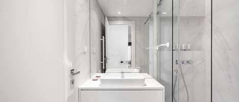 Un baño moderno con ducha de vidrio, tocador blanco con lavamanos grande y espejo sobre el tocador.