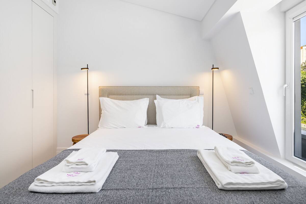 Una camera d'albergo moderna con un letto grande, due comodini e vista dalla finestra.