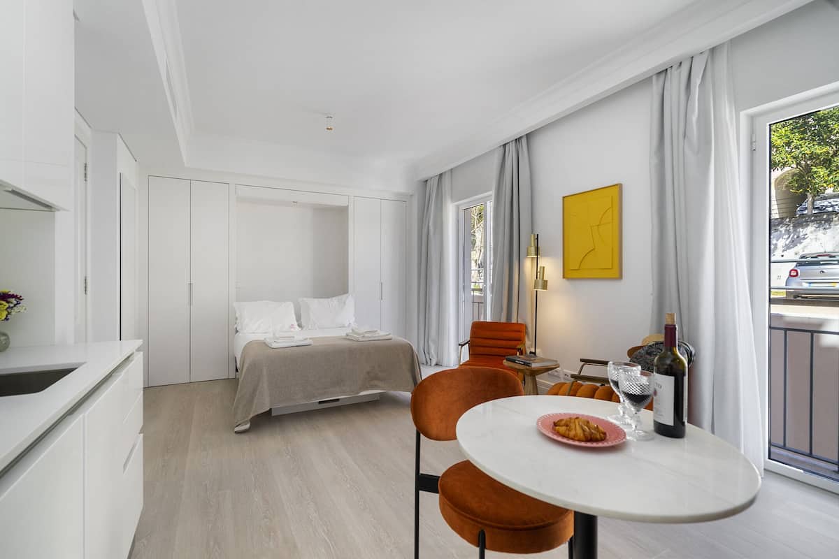 Una camera d'albergo moderna con un letto, un'area pranzo con tavolo e sedie, e vista all'esterno.