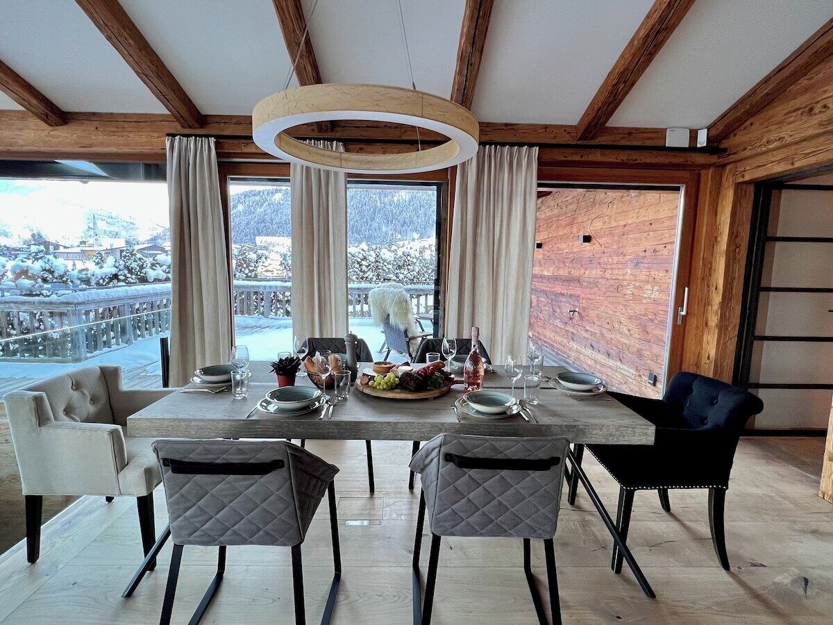 Un comedor con una mesa dispuesta para cuatro, techo de madera y vistas a un paisaje nevado.