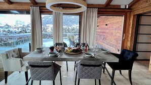 A dining area with a table set for four, a wooden ceiling, and a view of a snowy landscape. - Hideaway Design Chalet (Reith bei Kitzbühel)