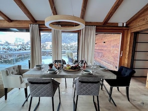 A dining area with a table set for four, a wooden ceiling, and a view of a snowy landscape.