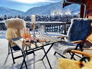 Ett bord uppdukat utomhus med en vacker utsikt över bergen, en träbänk och en stol täckt med fäll.