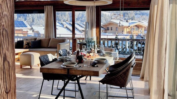 A dining area with a wooden table, chairs, and a view of a snowy mountain landscape. - Hideaway Design Chalet (Reith bei Kitzbühel)