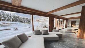 A modern interior with a large sectional sofa, wooden beams, and a view of a snowy landscape. - Hideaway Design Chalet (Reith bei Kitzbühel)