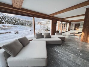 Un intérieur moderne avec un grand canapé d’angle, des poutres en bois et une vue sur un paysage enneigé.