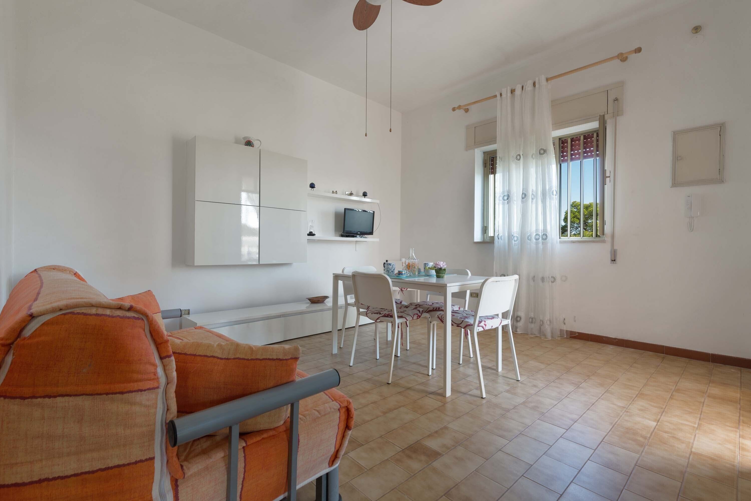A modern living room with a sofa, dining table, and chairs. There is a TV on a shelf, a window with curtains, and a tiled floor.