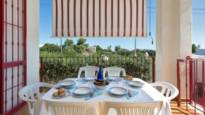 A balcony with a table set for dining, surrounded by white chairs, and a view of greenery and buildings in the background. - 3149 Villa Giovì - Appartamento 1 by Barbarhouse (Manduria)