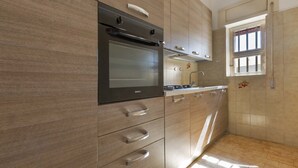 A modern kitchen with wooden cabinets, a built-in oven, and a window with a view. - 3149 Villa Giovì - Appartamento 1 by Barbarhouse (Manduria)