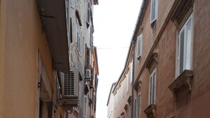 Une rue étroite avec des tables et des chaises installées à l’extérieur, sous des parasols jaunes, ce qui laisse supposer qu’il s’agit d’un café ou d’un restaurant.