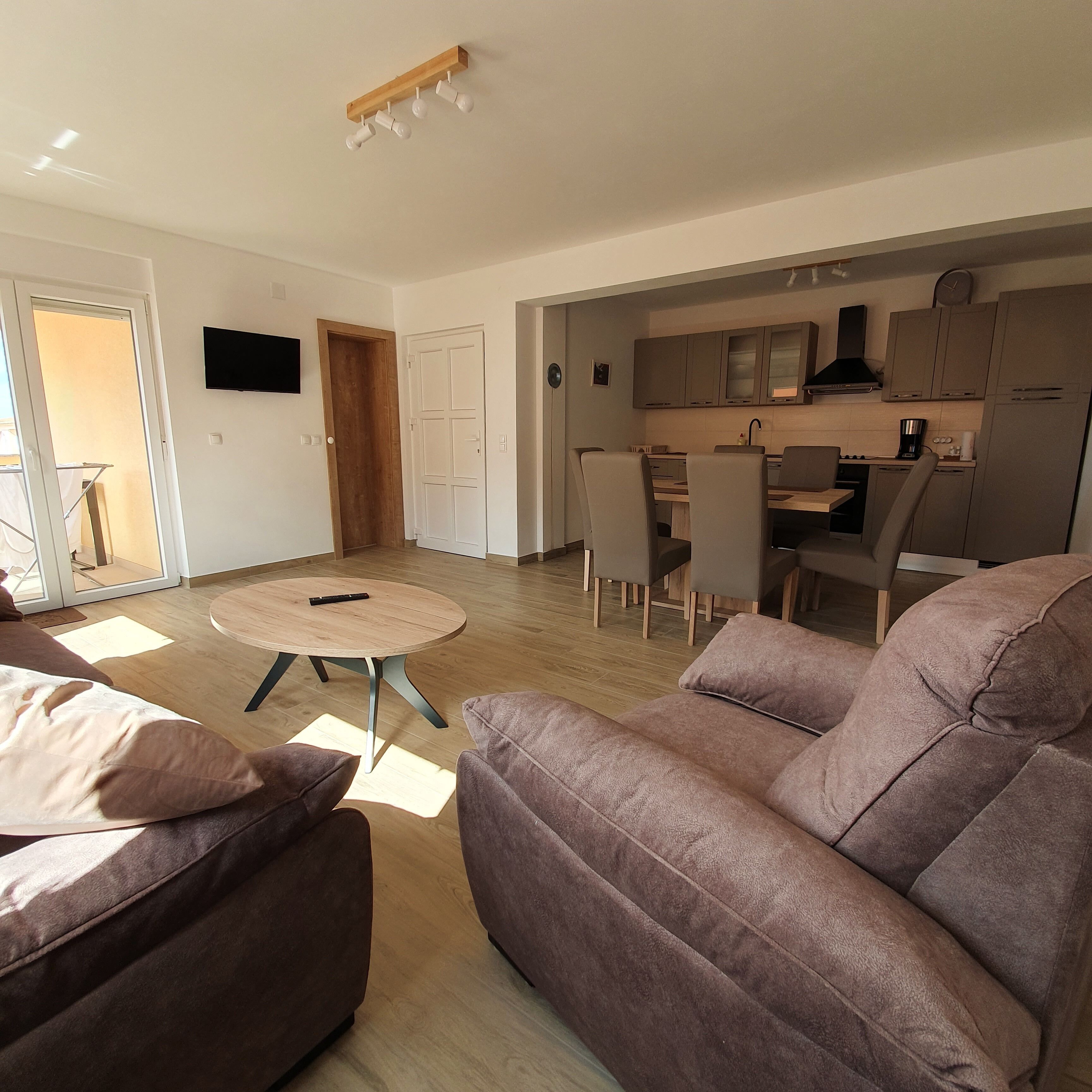A modern living room with a brown sofa, a round coffee table, and a dining area with a kitchen in the background.