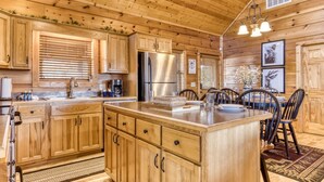 A wooden cabin-style kitchen with a central island, wooden cabinets, and a dining area with chairs. - Whiskey's mountain lodge, Mtn Views, Game Room, $560 FREE tickets each paid day (Sevierville)