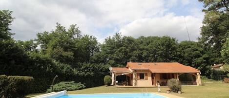 Une maison avec une piscine, entourée d’un jardin et d’arbres.
