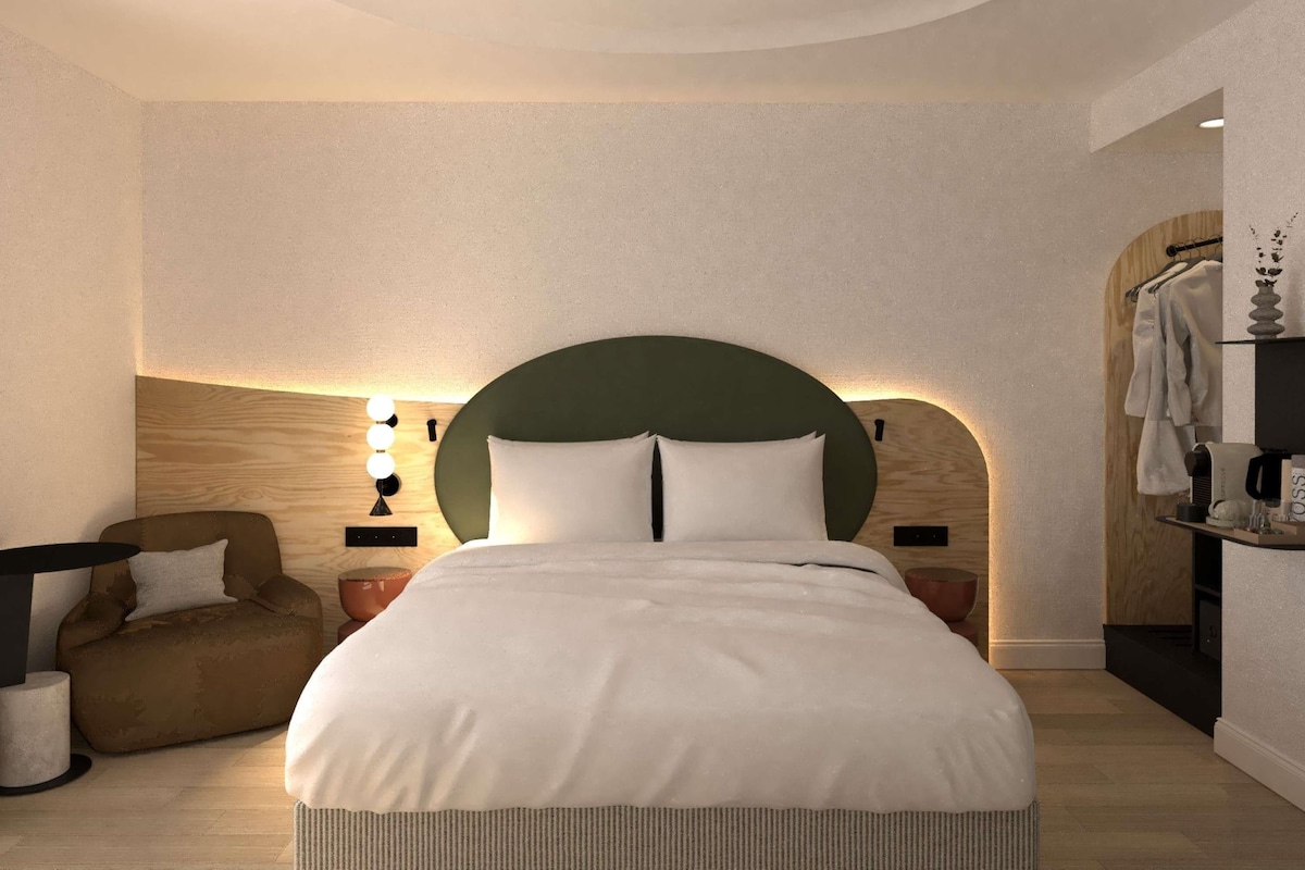 A modern hotel room with a large bed, a seating area, and a vanity with a mirror.