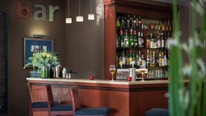 Una zona de bar con taburetes de madera, una estantería llena de licores y un cuadro en la pared.