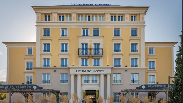 Un hotel de varios pisos con fachada amarilla, balcones y señalización que indica 'Le Parc Hotel' y 'Brasserie La Veranda'.
